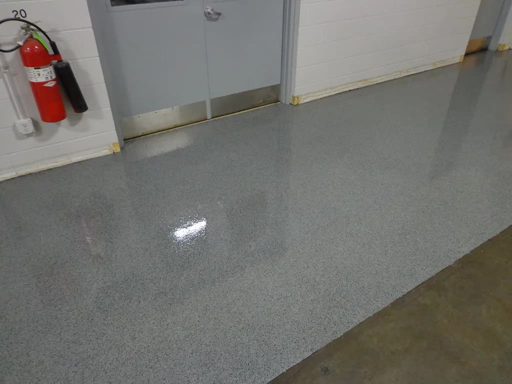 A grey flake epoxy floor with a gloss finish running along a commercial corridor past a set of double doors and a fire extinguisher.