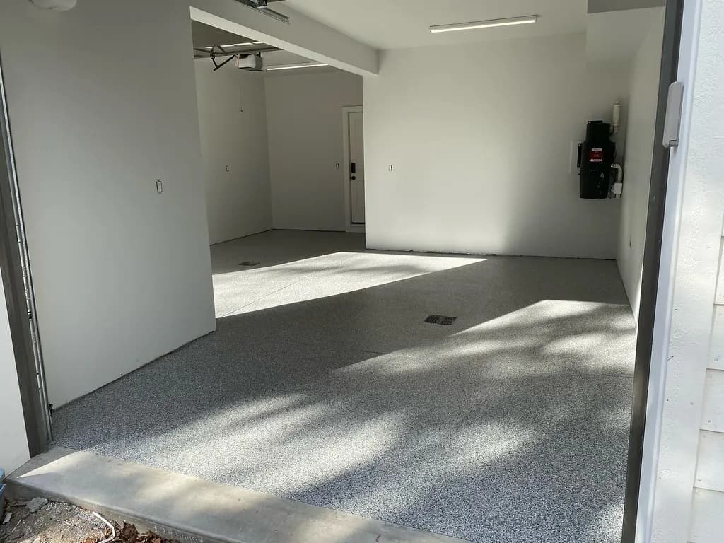 A residential double garage with a grey flake epoxy floor, seen from the open roller door, with afternoon sun across the floor.
